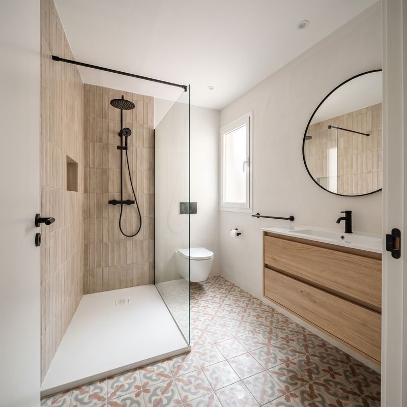 Baño reformado con azulejo beige vertical en la ducha, suelo de baldosa hidráulica y mueble de roble