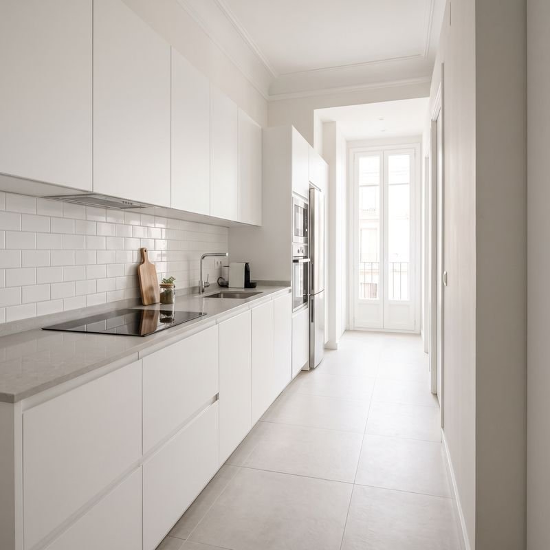 Cocina reformada en línea con muebles blancos sin tiradores, encimera gris y azulejo metro blanco
